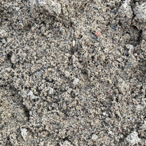 Close-up of loose, textured 0/2 recycled pipe bedding sand from Runfold, showing light brown and grey grains and small clumps.