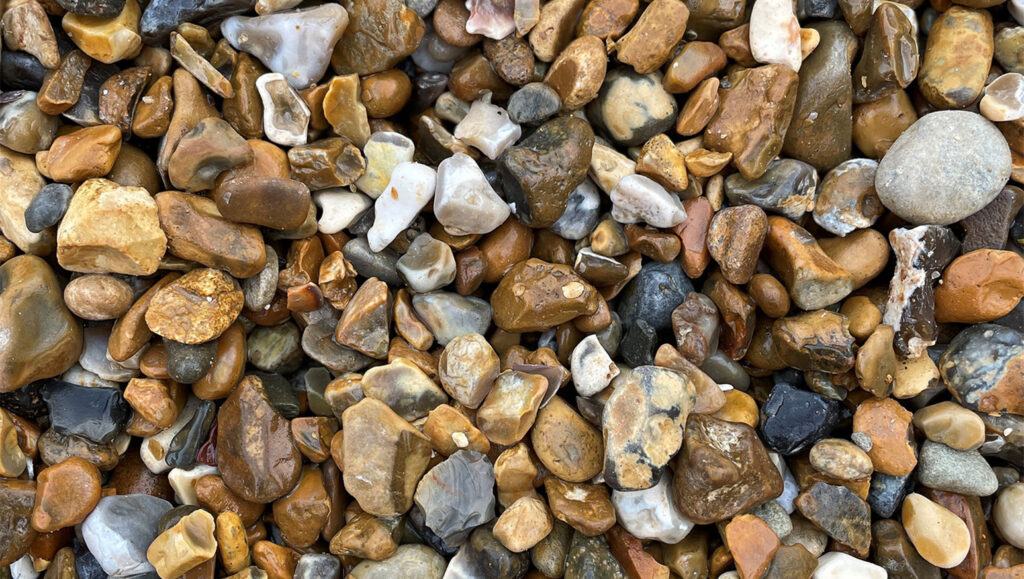 Close-up of 10-20mm gravel in Runfold, Farnham, Surrey with smooth brown, tan, grey, and white stones covering the ground.