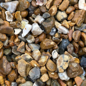 Close-up of 10-20mm gravel in Runfold, Farnham, Surrey with smooth brown, tan, grey, and white stones covering the ground.