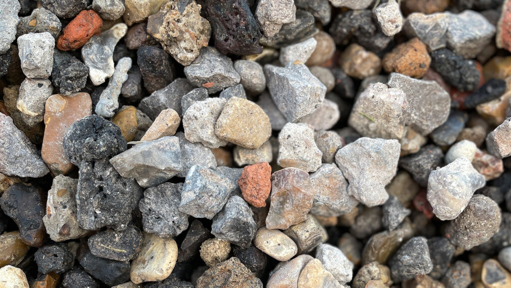 Close-up of 10/20 recycled aggregate from Runfold, Farnham: small, rough stones in grey, black, brown, and reddish tones.