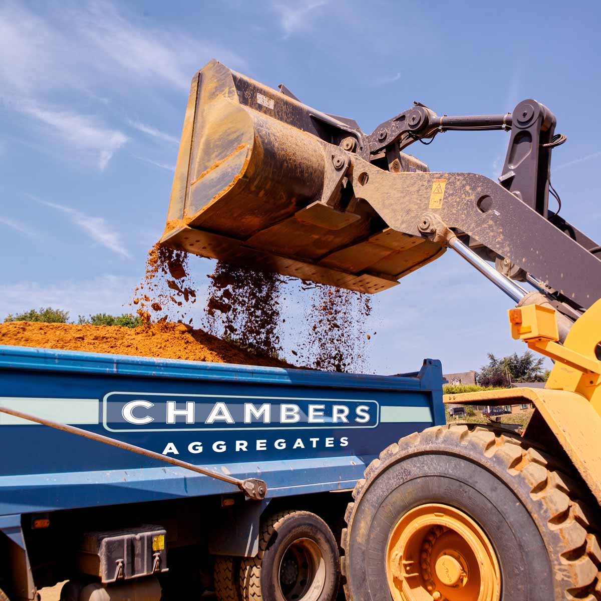 A construction vehicle pours soil into a blue "Chambers Aggregates" lorry at a site in Runfold, Farnham, Surrey.