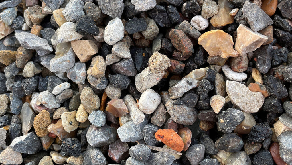 Close-up of 4/10 recycled aggregate from Runfold, Surrey; mixed grey, brown, black, and orange rocks and pebbles.