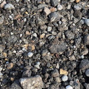 Close-up of rough asphalt road planings with uneven grey and brown stones, gravel, and debris in Runfold, Farnham, Surrey.