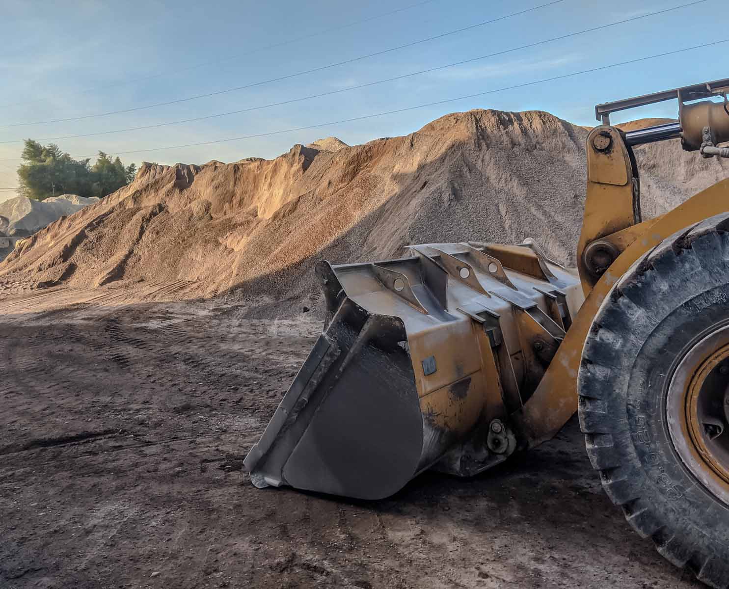 Yellow bulldozer with large bucket in front of sand or gravel pile at Runfold, Farnham, Surrey construction site; clear sky, trees behind.