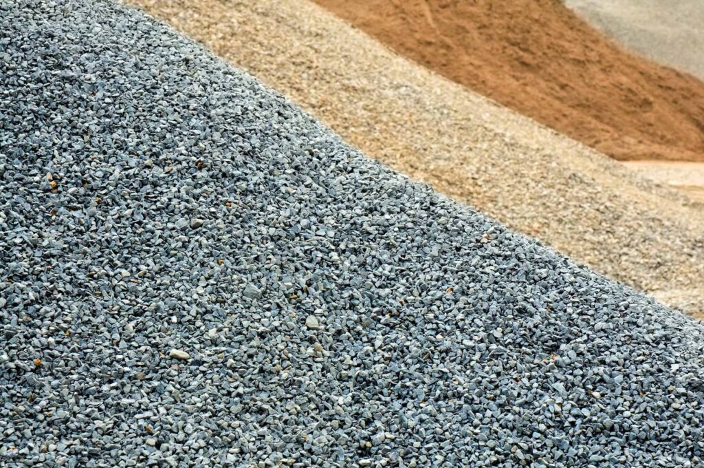 Piles of grey gravel, tan gravel, and reddish-brown soil at a construction site in Runfold, Farnham, Surrey.