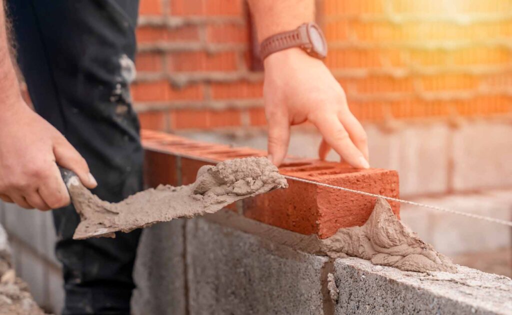 Bricklayer laying brick on cement mix on construction site close-up. Reduce the housing crisis by building more affordable houses concept